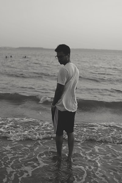 白天，一名身穿白衬衫和黑短裤的男子站在海滩上